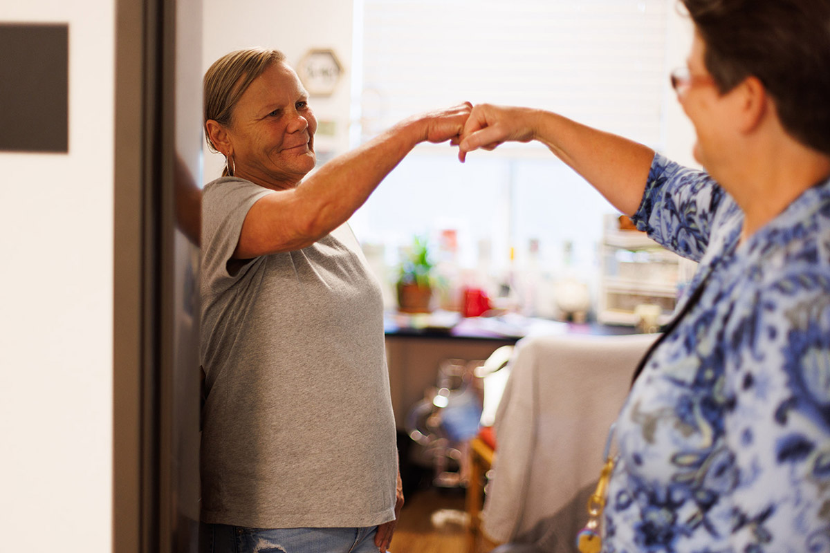 two women give each other a supportive fist bump in the doorway of a room at Pauls Place housing community in Davis CA
